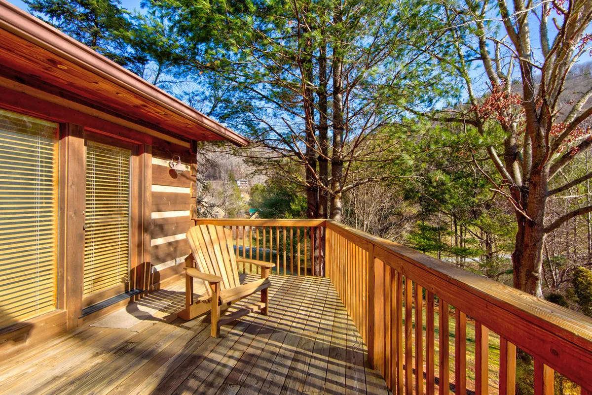 A calm and inviting wooden deck with an Adirondack chair, surrounded by natural greenery. The deck opens out into a usable outdoor space, ideal for relaxing and enjoying the fresh mountain air. The tranquil atmosphere hints at a spacious area where dogs could play or rest comfortably beside their owners.