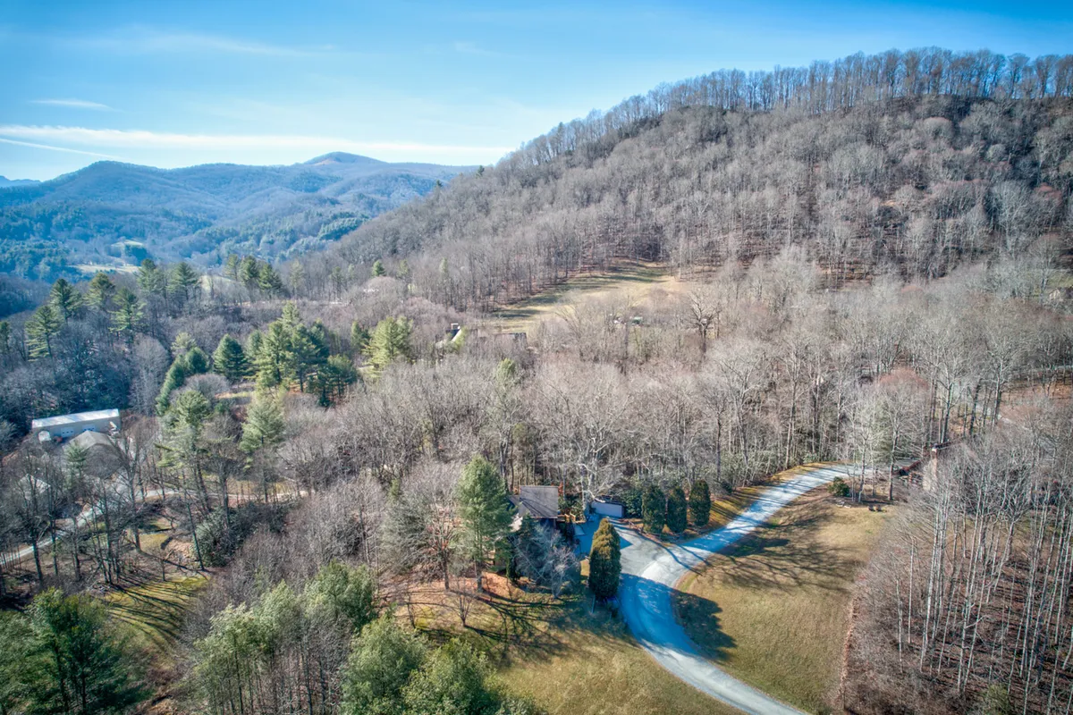 A tranquil view featuring the cabin nestled among trees, with a winding driveway leading to the home. The surrounding natural landscape hints at nearby trails and the peaceful, rural setting.