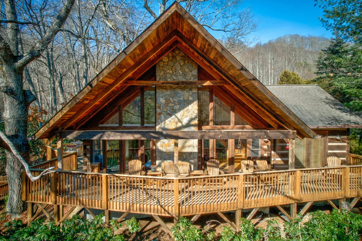 A welcoming deck area with Adirondack chairs, stone chimney, and large windows looking out over the trees. The setting invites gatherings with friends, cozy moments with sunrise coffee, or unwinding after mountain adventures. The inviting deck and natural surroundings reflect all-season fun and relaxation.