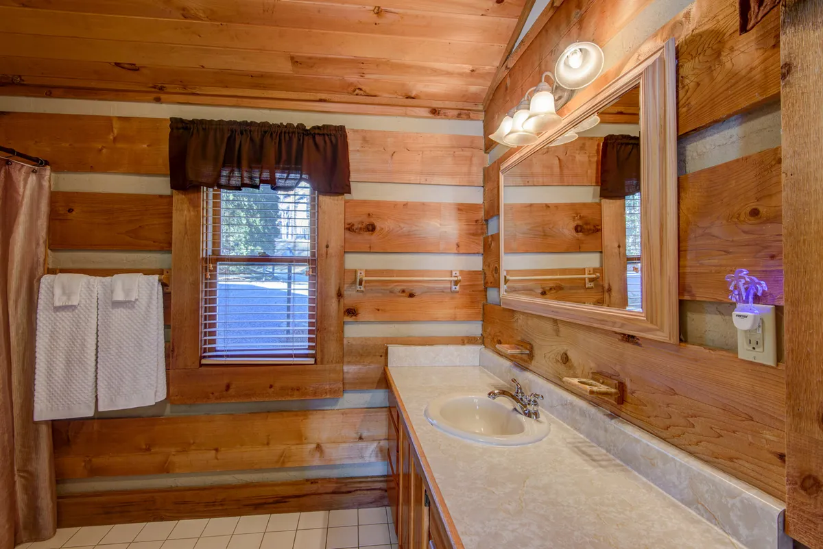 A bathroom with inviting wood-paneled walls, a modern vanity and sink, a well-lit mirror, and a window that brings in soft natural light. Fresh towels and subtle decor create a spa-like, comfortable atmosphere.