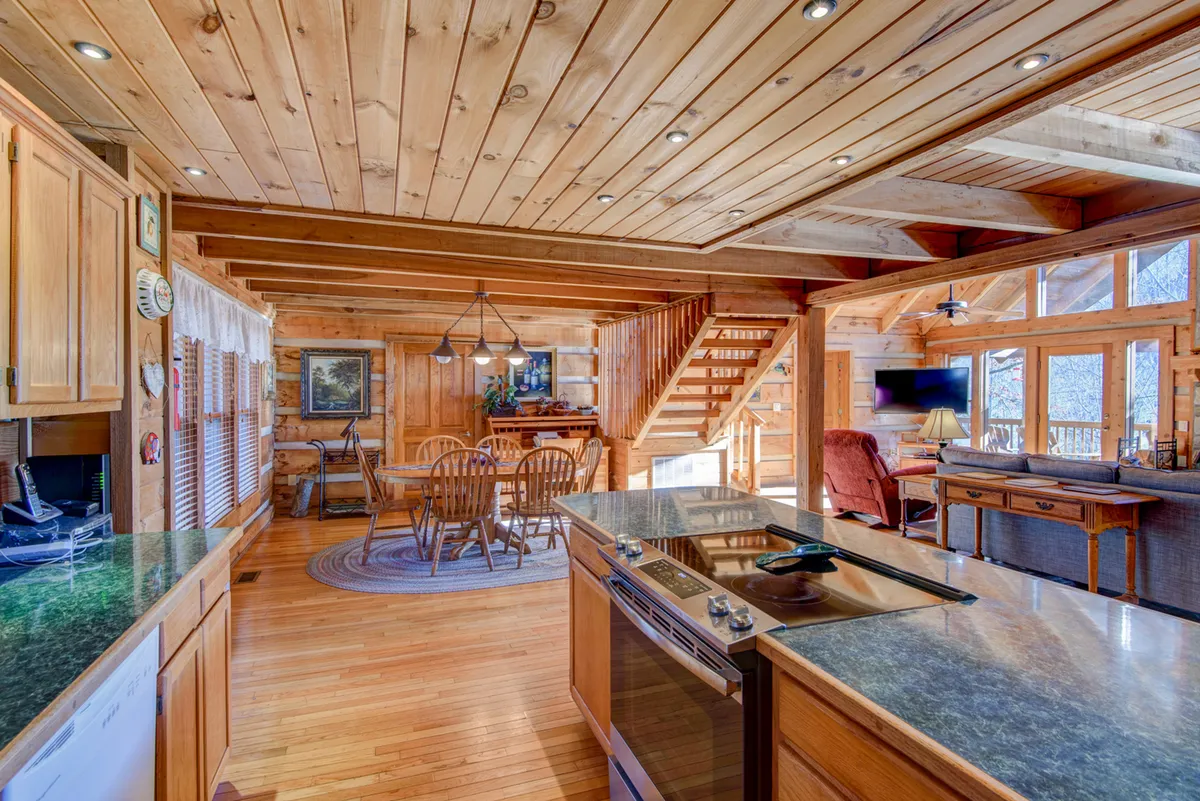This wide-angle interior shot displays the seamless flow between the kitchen, dining area, and living space. The kitchen island, dining table, and staircase are all visible, illustrating how these spaces are interconnected and suitable for group activities, conversation, and relaxation.