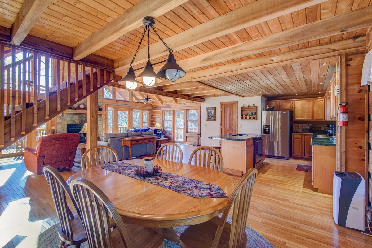 This image focuses on the dining area, with a clear view of the table, staircase, kitchen, and living room in the background. The scene suggests activities like family meals, celebrations, or simply enjoying a meal after a day exploring.