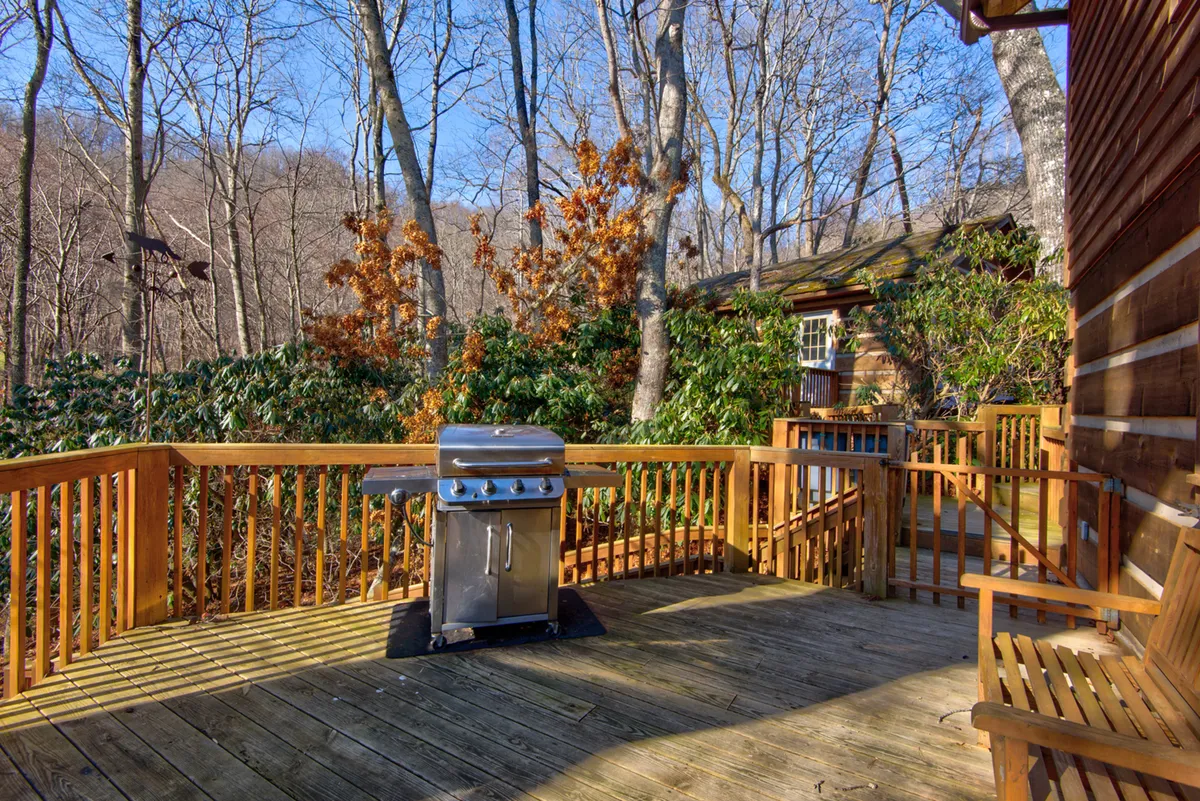 A view of the wooden deck featuring a BBQ grill, surrounded by trees and set with a bench for seating. The scene is relaxed and perfect for entertaining or simply enjoying the outdoors.