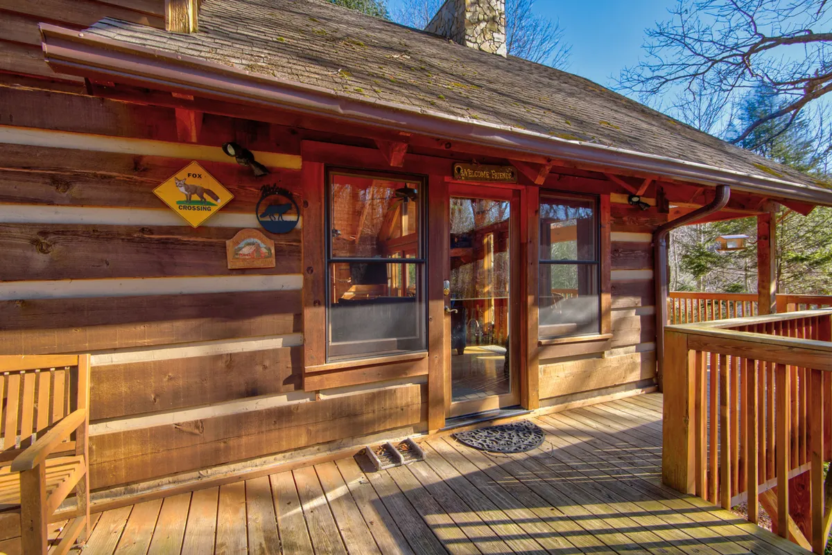 A welcoming log cabin entrance with a wooden deck, a friendly welcome sign, and bench seating. The porch sets a tone of hospitality and comfort, suggesting a home that happily receives both people and their pets after a day of exploring trails and parks.