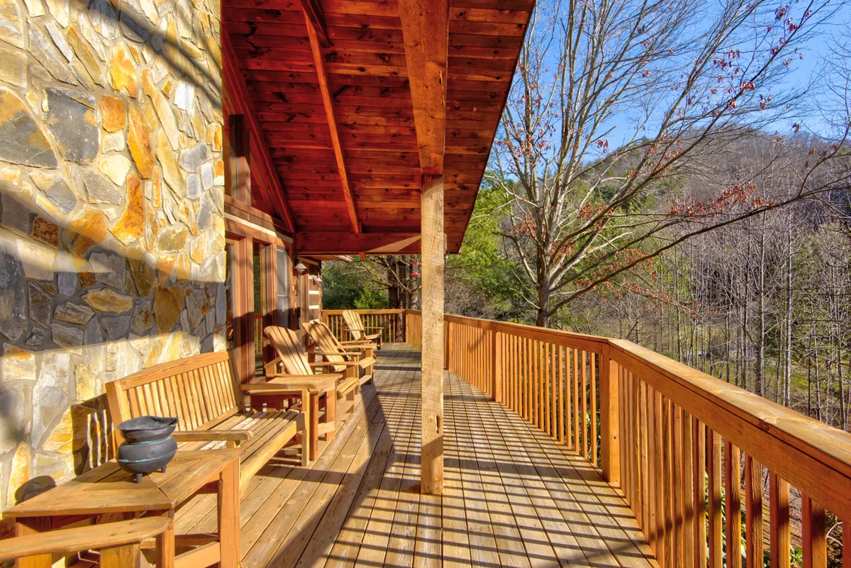 This image features a tranquil deck area with comfortable outdoor seating nestled against a stone wall, flanked by adjoining trees. The atmosphere is serene, perfect for enjoying a book, quiet conversation, or simply watching the sunset over the mountains.
